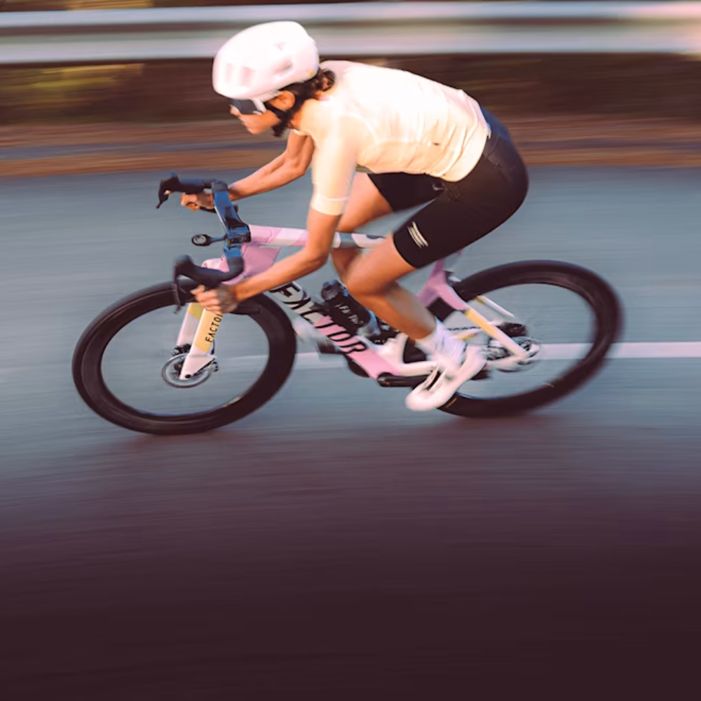 Ciclista rodando en carretera con bicicleta Factor ONE Blush, imagen de acción con fondo en movimiento