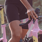 Detalle del cockpit y el cuadro rosa de la bicicleta Factor ONE Blush mientras la ciclista sujeta el manillar