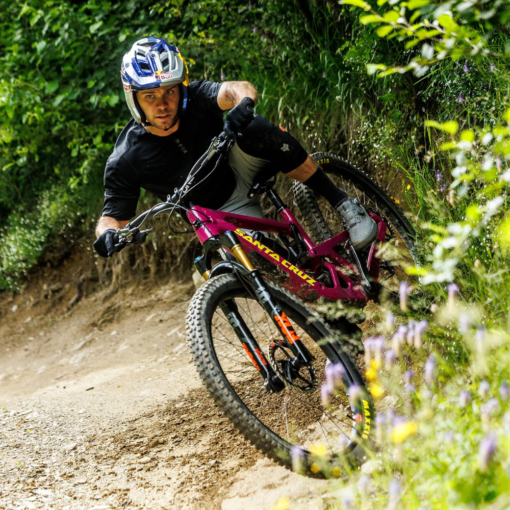 Ciclista descendiendo por un sendero sobre una bicicleta Santa Cruz Bronson V5 rosa.