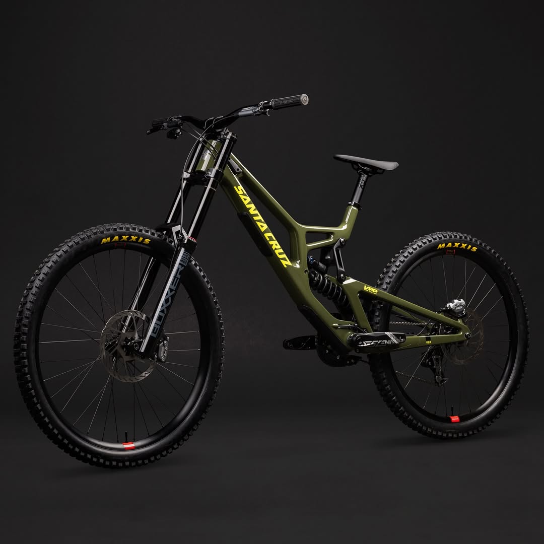 Bicicleta Santa Cruz V10 verde oliva en perspectiva trasera de tres cuartos sobre fondo oscuro.