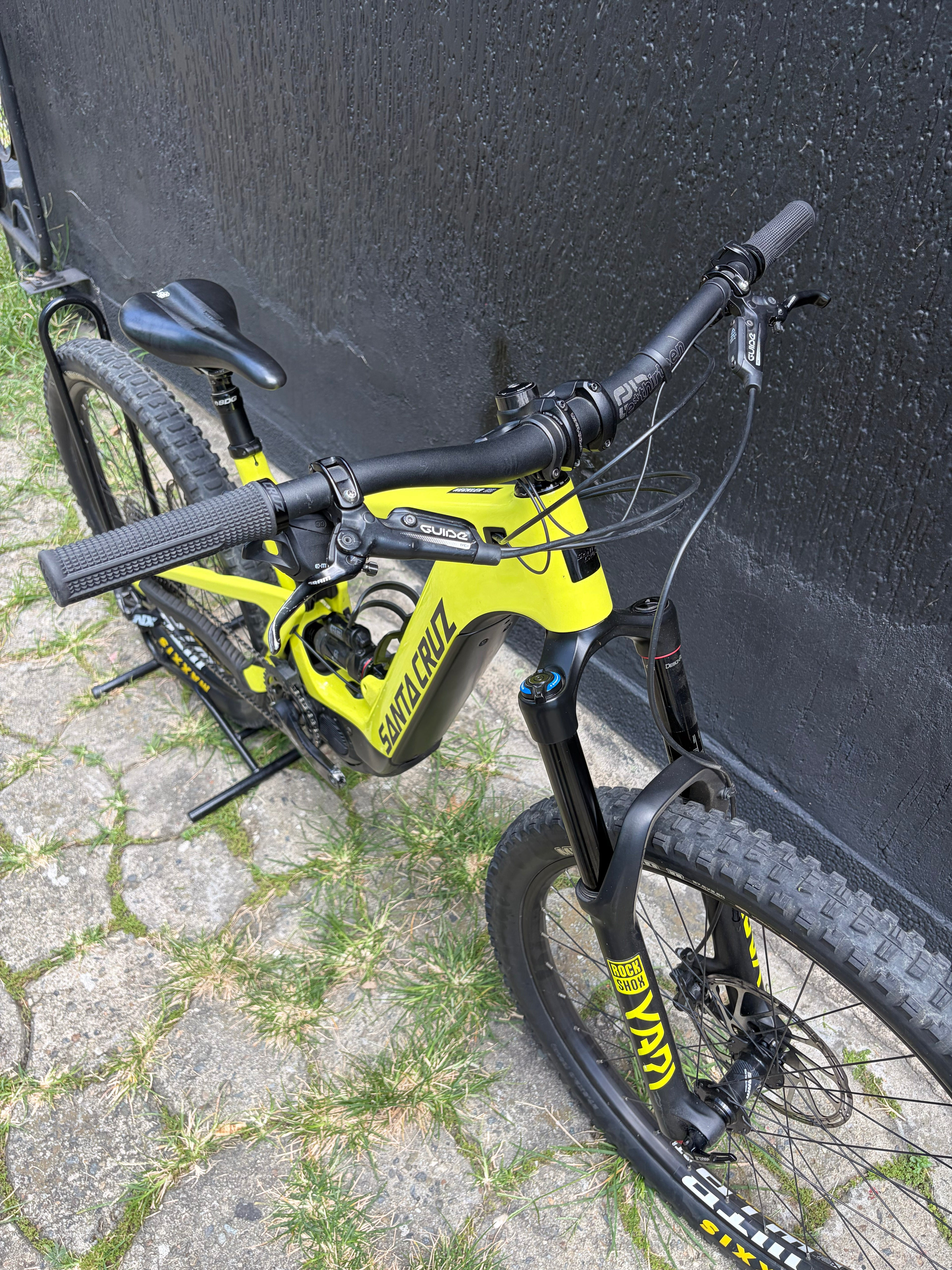 Bicicleta usada Santa Cruz Heckler 8 verde lima en perspectiva frontal junto a una pared oscura.