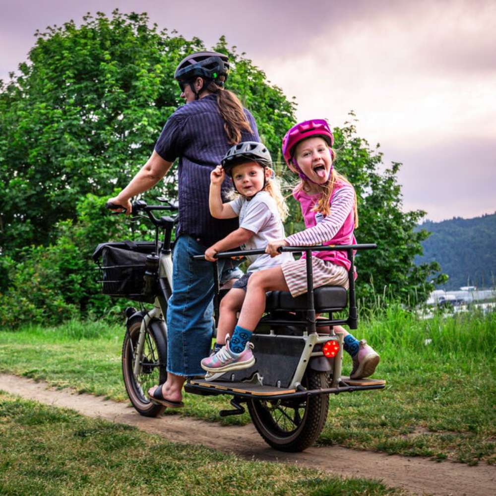 Adulto y dos niños usando cascos Smith Sidekick Jr Matte Black y Matte Lollipop Fade en bicicleta de carga