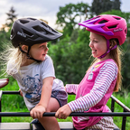Dos niños conversando mientras usan cascos Smith Sidekick Jr Matte Black y Matte Lollipop Fade al aire libre