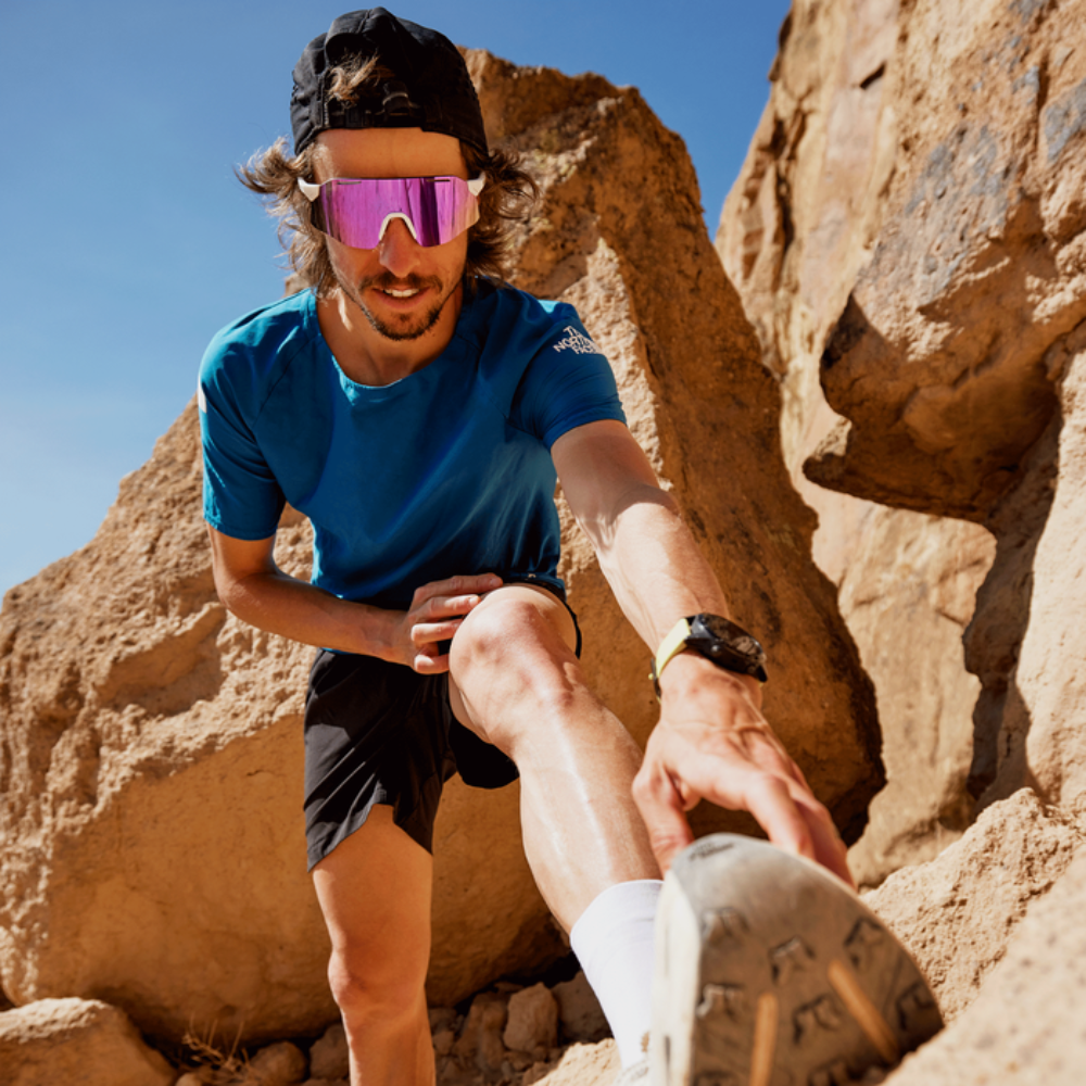 Corredor de trail usando gafas Smith Vert Running blancas con lente violeta espejo ChromaPop entre formaciones rocosas